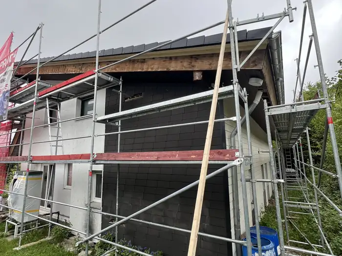 Fertige Fassade mit Holzgiebel und neuem Dach hinter dem Gerüst