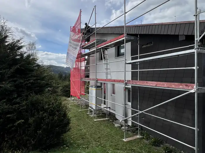 Eingerüstetes Wohnhaus in Hanglage mit Werbefahne am Gerüst