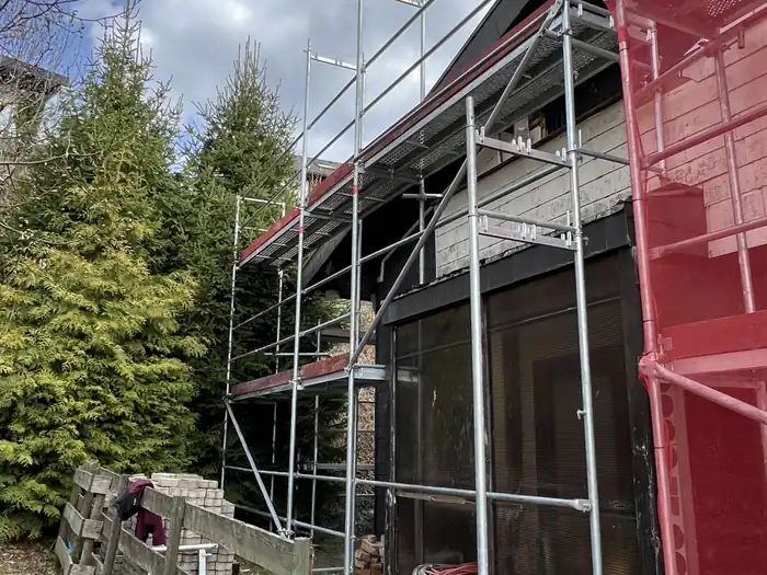 Dunkle Fassadenverkleidung mit Holzgiebel hinter dem Gerüst