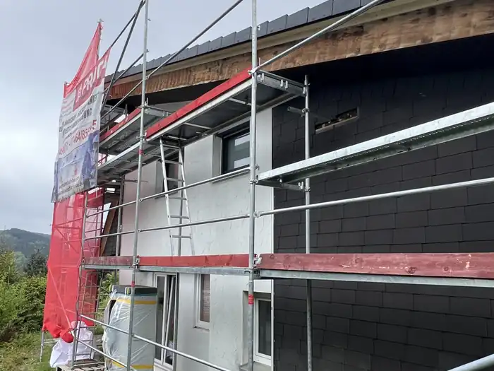 Dunkle Plattenfassade über hellem Sockelbereich, Gerüst davor